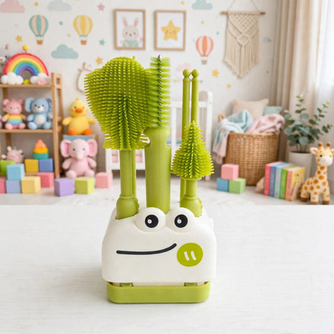 A green and white baby toothbrush holder set with three toothbrushes and two cleaning brushes, featuring a cute cartoon face on the front, set against a softly blurred nursery background.
