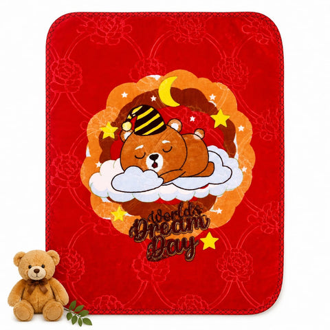 A red plush blanket with rounded corners featuring a cartoon bear sleeping on a cloud with the text 'World's Dream Day' and a crescent moon and stars. A small teddy bear and green leaves are placed at the bottom left on a white background.