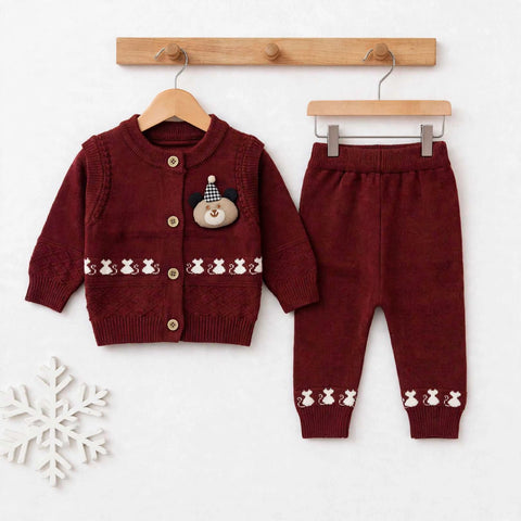 A baby clothing set consisting of a burgundy knit cardigan sweater and matching pants, displayed on wooden hangers against a white background with a wooden peg rail and a decorative snowflake.