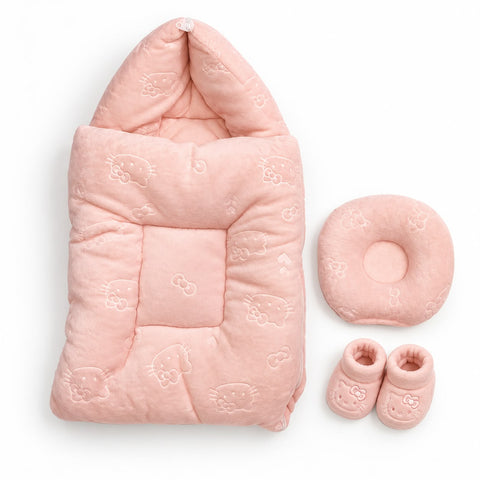 A pink baby bedding set on a white background, including a padded hooded swaddle blanket with an embossed Hello Kitty pattern, a matching round cushion, and a pair of soft booties.