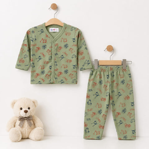 A two-piece baby outfit set consisting of a short-sleeve button-front cardigan and matching pants in sage green with a colorful dinosaur print, displayed on wooden hangers next to a cream teddy bear.