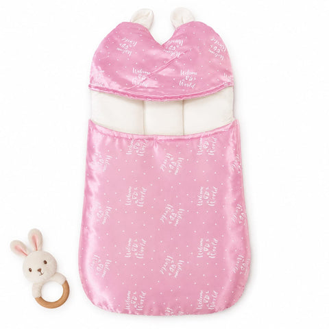 A pink baby sleep bag with white bunny and star patterns, featuring a soft white inner lining and two white bunny ears at the top. A small plush bunny teething ring toy is placed to the left on a clean white background.