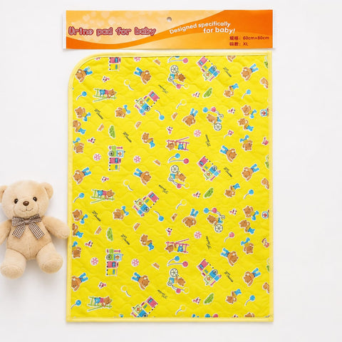 A yellow quilted baby urine pad with a colorful cartoon bear pattern, shown with its orange header card packaging and a small teddy bear toy on a white background.