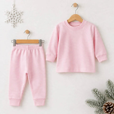 A two-piece baby clothing set in light pink, featuring a long-sleeve crewneck top and matching jogger pants, displayed on wooden hangers against a light background with seasonal decorative props.
