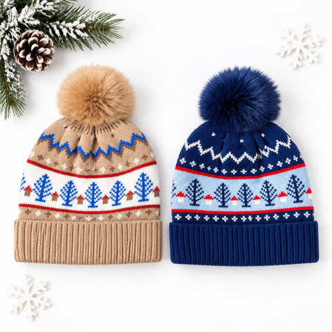 Two winter knit beanies with fluffy pom-poms are displayed on a white background with holiday props. The left hat is tan with a brown pom-pom and a multicolor Nordic tree pattern.