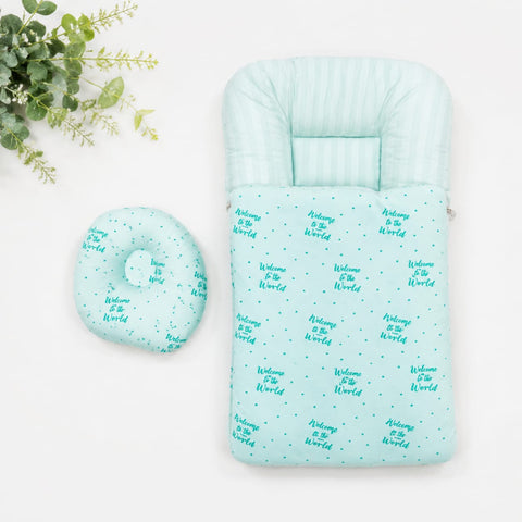 A baby sleeping bag and matching ring pillow in mint green with a repeating 'Welcome to the World' text and star pattern, displayed on a white background with a decorative green plant in the corner.