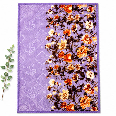 A rectangular purple area rug with a floral pattern, laid flat on a white background with a green eucalyptus branch on the left side.