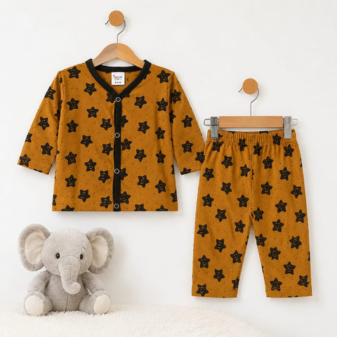 A baby clothing set consisting of a long-sleeve button-front cardigan and matching pants in mustard yellow with a black star pattern, displayed on wooden hangers against a white wall, with a plush gray elephant toy at the bottom left.