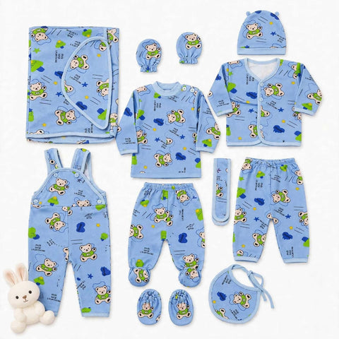A baby clothing set laid out on a white background, including a light blue long-sleeve top, matching pants, bib, hat, booties, swaddle, and overalls, all printed with a playful cartoon bear and cloud pattern. A small white plush bunny is placed at the lower left.