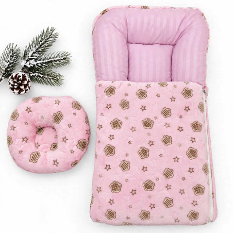 A pink baby sleeping bag set with a matching circular cushion, styled with a pine branch and pinecone on a white background.