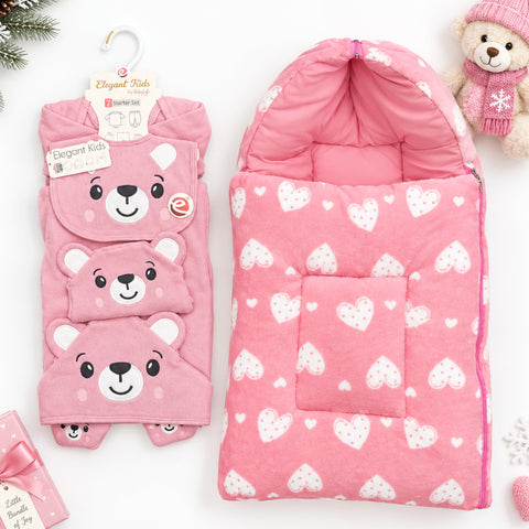 Pink children's bedding set from Elegant Kids, featuring a hooded sleep bag with a white heart pattern and a matching sleep mask with a bear face design, displayed on a white background with a teddy bear toy.