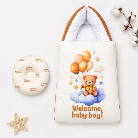 A baby welcome gift set featuring a cream-colored padded tote bag with a teddy bear graphic and the text 'Welcome, baby boy!' alongside a matching round padded cushion, styled on a white background with decorative cotton and star props.