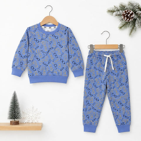 A children's two-piece sweatshirt and jogger pants set in a dusty blue color, decorated with a repeating pattern of gold and navy glasses. The sweatshirt is shown on a wooden hanger on the left, and the matching pants are shown on a metal hanger on the right.