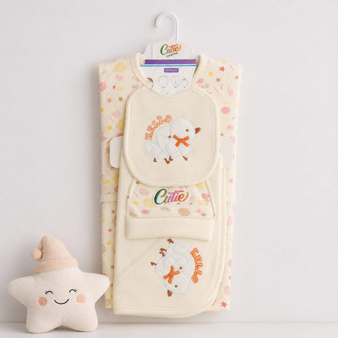 A folded baby clothing set in cream with pastel pink, yellow, and orange star and swirl patterns, featuring a matching bib, footed mitt, and wrap with embroidered cartoon duck motifs and the word 'Cuteo'. A small plush star toy sits to the left on a white background.