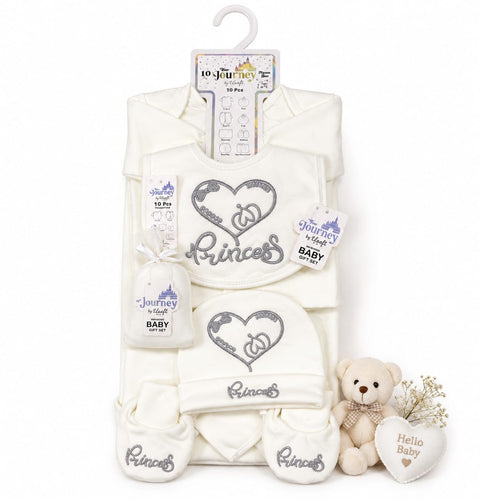 A baby clothing gift set on a white background, featuring an off-white/cream 10-piece outfit set with silver glittery 'Princess' and heart designs, a small plush teddy bear, and a heart-shaped 'Hello Baby' pillow.