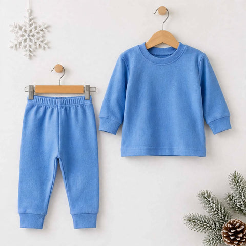 A two-piece children's outfit set consisting of a light blue long-sleeve top and matching light blue pants, displayed on wooden hangers against a light beige wall with seasonal decorative props.