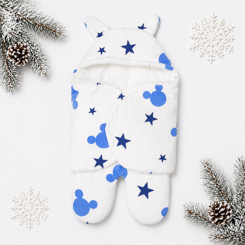 A white footed baby wrap or swaddle with blue Mickey Mouse head silhouettes and blue stars, styled flat-lay on a white background with decorative snowflakes and pine branches.