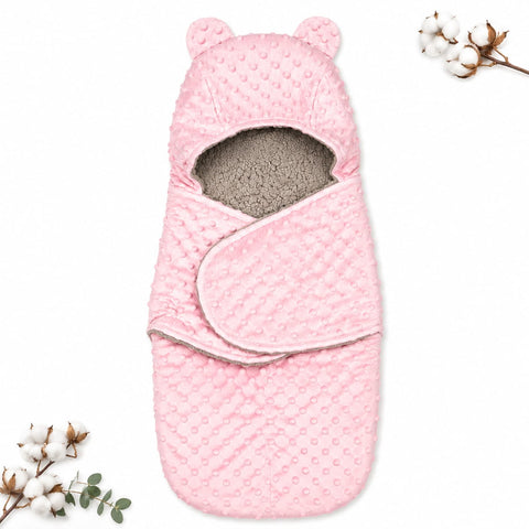 A pink baby swaddle wrap with a textured minky dot pattern, featuring bear ears on the hood and a soft gray fleece lining, displayed on a white background with decorative cotton stems.