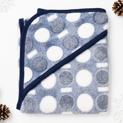 A folded fleece blanket with a blue-gray and white polka dot pattern and navy blue trim, styled on a white background with decorative pinecones in the corners.