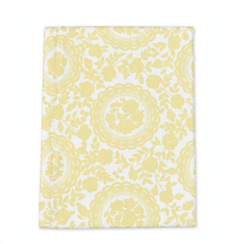 A rectangular white fabric item, likely a tea towel or napkin, featuring a repeating light yellow floral and circular lace-like pattern, shown flat against a white background.