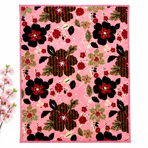 A square textile product, likely a quilt or rug, featuring a vibrant pink background with a repeating floral pattern of black, red, and olive green flowers. The textile is displayed flat against a white background with a decorative cherry branch on the left side.