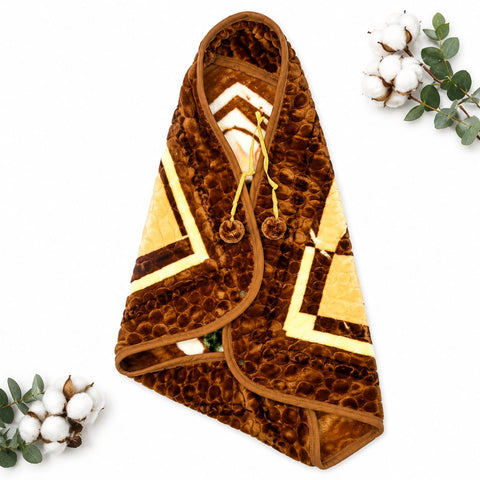 A brown textured hooded blanket or throw with cream and dark brown geometric patterns, laid flat on a white background with decorative cotton and eucalyptus sprigs in the corners.