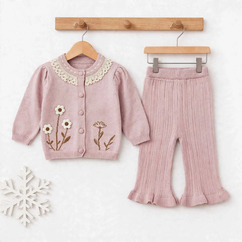 A toddler girl's two-piece knit outfit set consisting of a dusty pink cardigan with white lace collar and embroidered flowers, paired with matching pleated pink pants, displayed on wooden hangers against a white background.