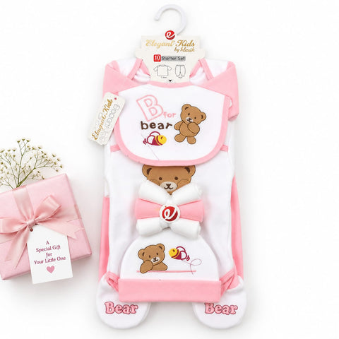 A baby footed sleeper set by Elegante Kids by Heart, featuring a white and pink design with embroidered brown teddy bears, a bow, and a bee. The set includes a footed sleeper and a matching bib, displayed on a hanger next to a pink gift box with baby's breath.